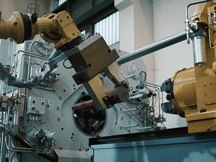 Ein gelber Roboterarm bei der automatischen Bestückung einer Rotationsschmiedeanalge mit einem Werkstück.